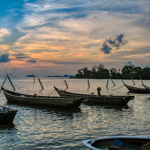 fishing boats anchored near the water's edge under a sunset sky